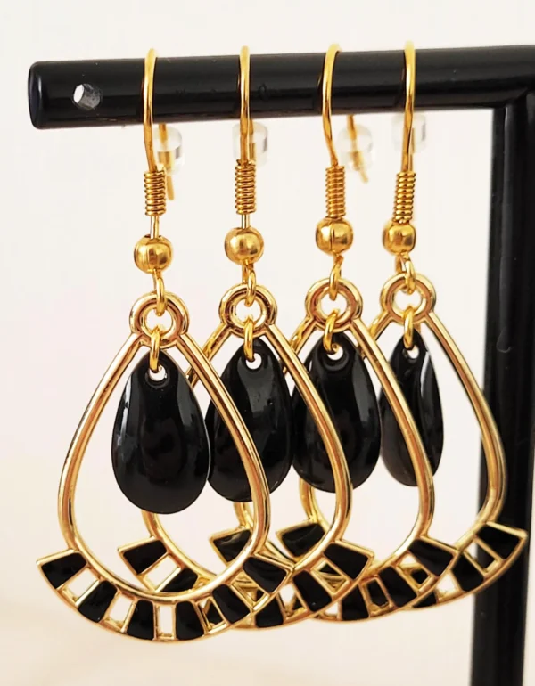 Boucles d'oreilles noires et dorées, légères à porter, en forme de gouttes, avec une pampille noire au milieu et des crochets pour attaches.