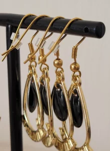 Boucles d'oreilles noires et dorées, légères à porter, en forme de gouttes, avec une pampille noire au milieu et des crochets pour attaches. Un caoutchouc est ajouté à l'arrière pour éviter de les perdre.