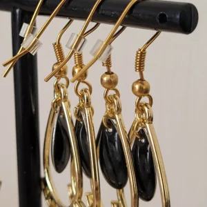 Boucles d'oreilles noires et dorées, légères à porter, en forme de gouttes, avec une pampille noire au milieu et des crochets pour attaches. Un caoutchouc est ajouté à l'arrière pour éviter de les perdre.