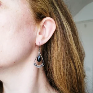 Boucles d'oreilles pendantes, en forme de gouttes noires et argentées avec une pampille noire au centre.