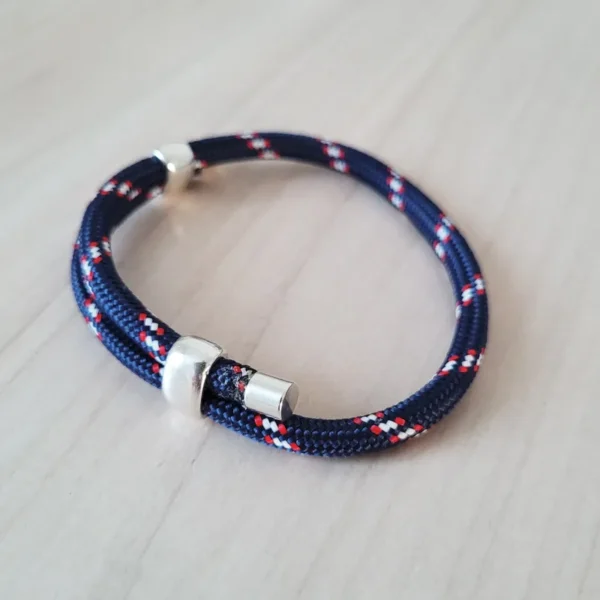 Bracelet coulissant en paracorde (ou corde) bleu marine, avec des dessins blancs et rouges réguliers, 2 poussoirs pour régler le bracelet et 2 embouts en métal à chaque bout.