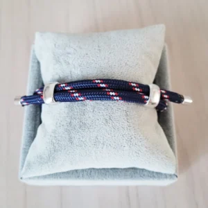 Bracelet coulissant en paracorde (ou corde) bleu marine, avec des dessins blancs et rouges réguliers, 2 poussoirs pour régler le bracelet et 2 embouts en métal à chaque bout.