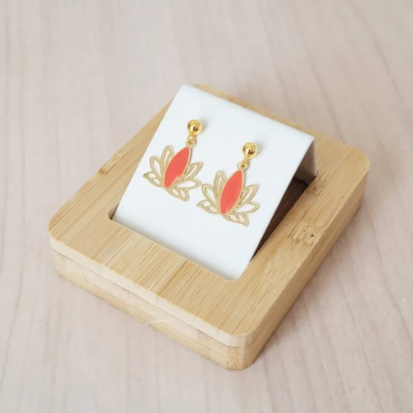 Clous d'oreilles dorées avec un pendant en forme de lotus ajouré de couleur doré et corail.