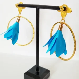 Boucles d'oreilles pendantes avec des supports en formes de 3 coeurs colorés en bleu et dorés. Ces supports ont un anneau martelé et un pompon en imitation satin de couleur bleu à l'intérieur.