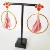 Boucles d'oreilles pendantes avec des supports en formes de 3 coeurs colorés en prune nacrée et dorés. Ces supports ont un anneau martelé et un pompon en imitation satin de couleur rose à l'intérieur.