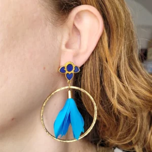 Boucles d'oreilles pendantes avec des supports en formes de 3 coeurs colorés en bleu avec résine Epoxy vitrail et dorés. Ces supports ont un anneau martelé et un pompon en imitation satin de couleur bleu à l'intérieur.