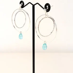 Boucles d'oreilles argentées avec 2 cercles imbriqués de tailles différentes et une perle de verre de Bohème en forme de goutte de couleur bleu translucide. Le support est un clou d'oreille en argent.