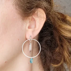 Boucles d'oreilles argentées avec 2 cercles imbriqués de tailles différentes et une perle de verre de Bohème en forme de goutte de couleur bleu. Le support est un clou d'oreille en argent. Photo avec la boucle d'oreille portée.