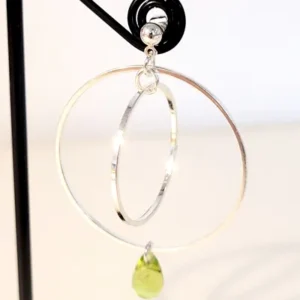 Boucles d'oreilles argentées avec 2 cercles imbriqués de tailles différentes et une perle de verre en forme de goutte de couleur vert translucide. Le support est un clou d'oreille en argent.