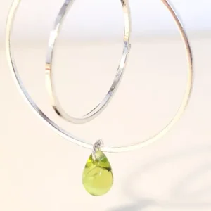 Boucles d'oreilles argentées avec 2 cercles imbriqués de tailles différentes et une perle de verre en forme de goutte de couleur vert translucide. Le support est un clou d'oreille en argent.