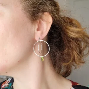 Boucles d'oreilles argentées avec 2 cercles imbriqués de tailles différentes et une perle de verre de Bohème en forme de goutte de couleur bleu. Le support est un clou d'oreille en argent. Photo avec la boucle d'oreille portée.