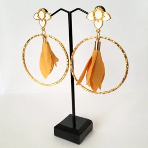 Boucles d'oreilles pendantes avec des supports en formes de 3 coeurs colorés en blanc et dorés. Ces supports ont un grand anneau martelé et un pompon en imitation satin de couleur moutarde à l'intérieur.